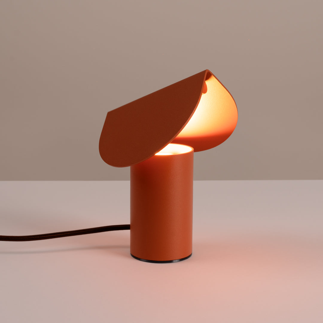 Lampe à poser BISCUIT ocre rouge allumée, sur une table