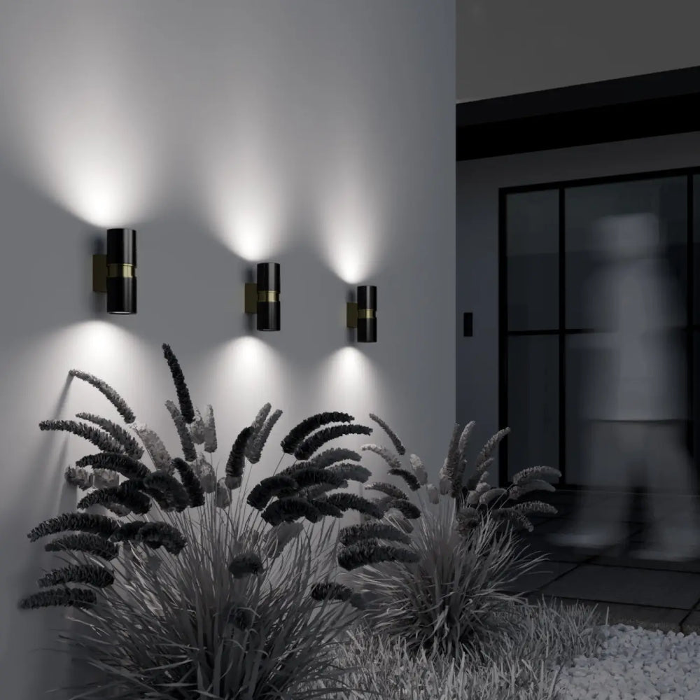 Trois appliques extérieure bowery cylindre double en métal noir avec accents dorés éclairent un espace moderne extérieur