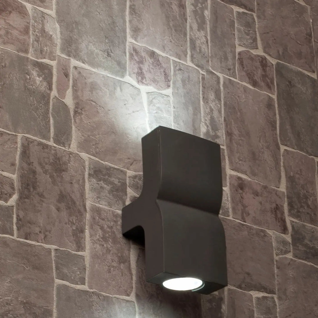 Applique Klamp gris foncé allumée sur un mur en pierre