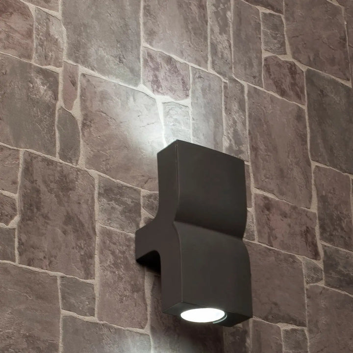 Applique Klamp gris foncé allumée sur un mur en pierre