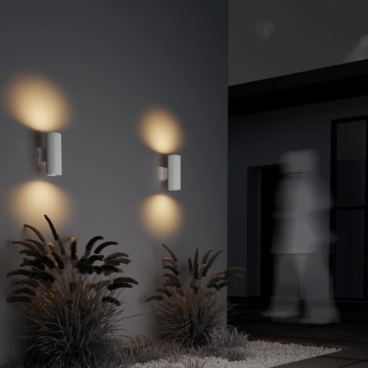 Deux appliques extérieure rando cylindre étanche blanches avec rainures verticales diffusant une lumière chaude sur mur gris