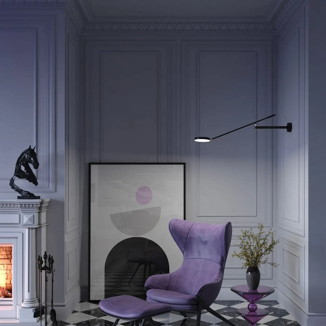 Applique murale long bras en métal noir avec tête ronde à côté d’un fauteuil en velours violet et ottoman assorti