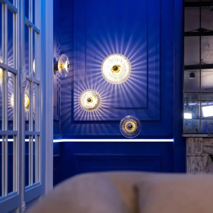 Trois appliques grace en verre soufflé avec centres dorés émettant une lumière radiante sur mur bleu profond