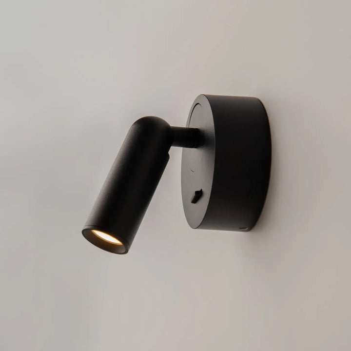 Applique liseuse mirax noire cylindrique avec tête ajustable et module rond émettant une lumière chaude