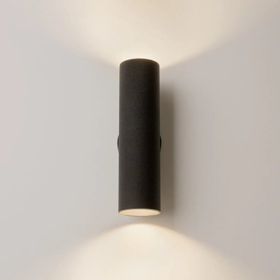 Applique murale artisan noire cylindrique avec surface texturée et éclairage d’accent chaleureux et focalisé