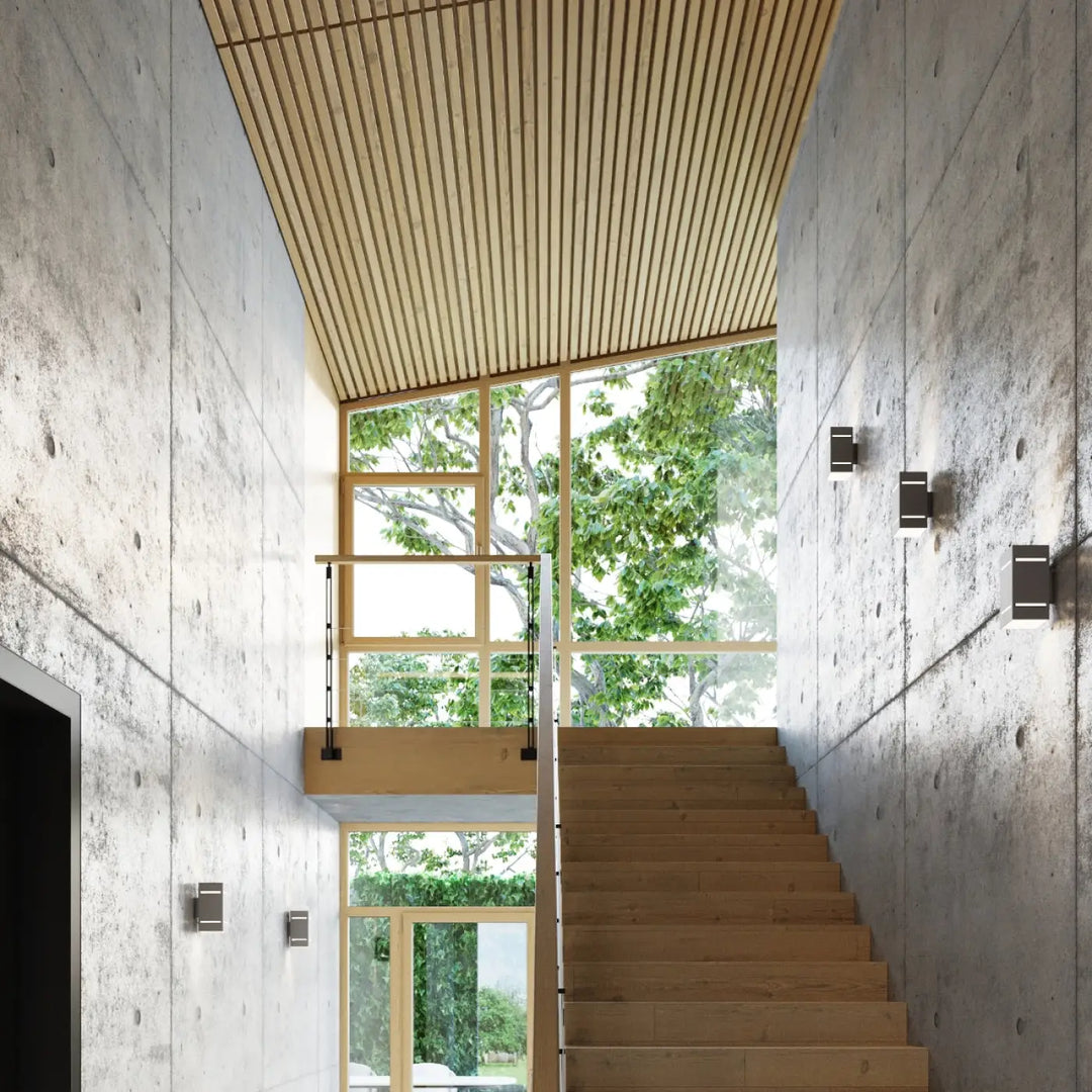 L’applique blocco gris avec spectacle lumineux et perforation linéaire sur un mur en béton texturé près d’un escalier en bois clair