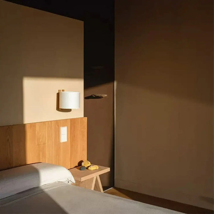 Applique murale moderne kaori avec abat-jour cylindrique blanc et base en bois diffusant une lumière douce en coin chambre