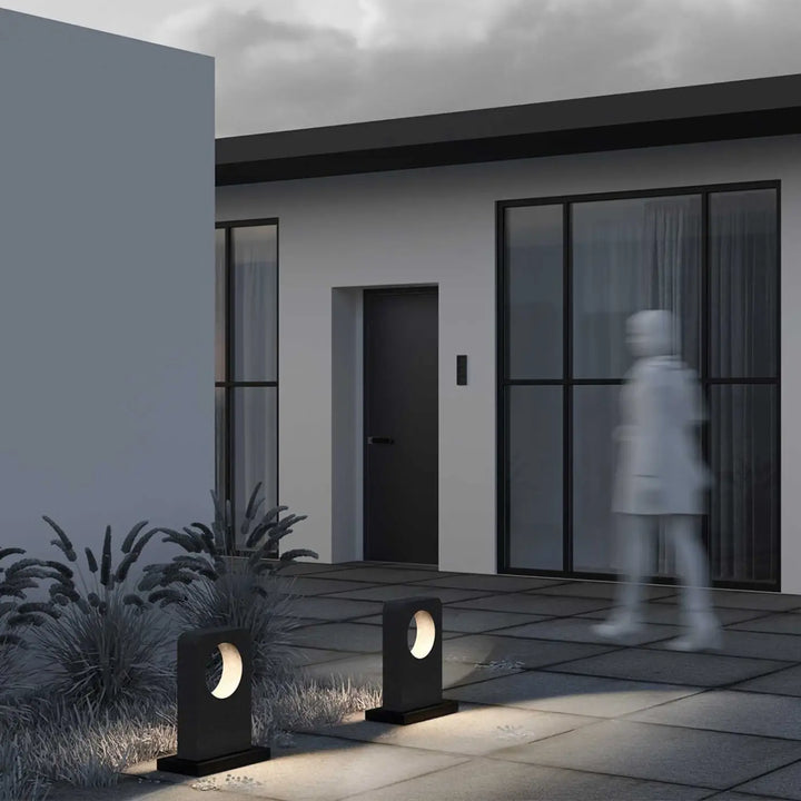 Borne extérieure en béton gris moderne avec découpes circulaires diffusant une lumière chaude le long d une allée
