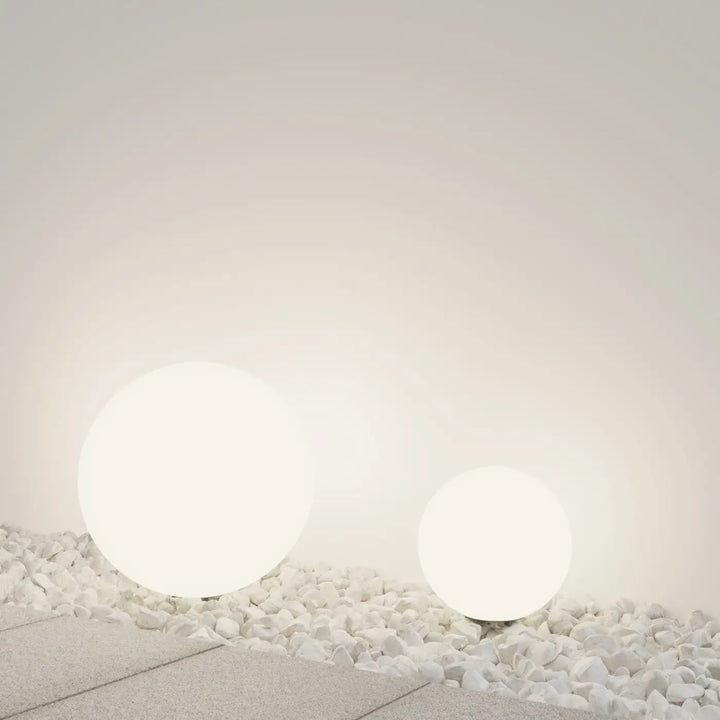 Deux boules lumineuses extérieures blanches en sphère opaline avec lumière douce posées sur des galets clairs