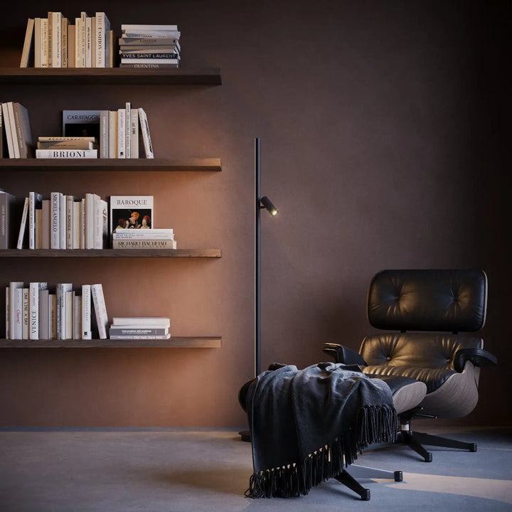 Lampadaire thin led à design ultra-fin placé à côté d’un canapé avec fauteuil eames lounge en cuir noir et chrome