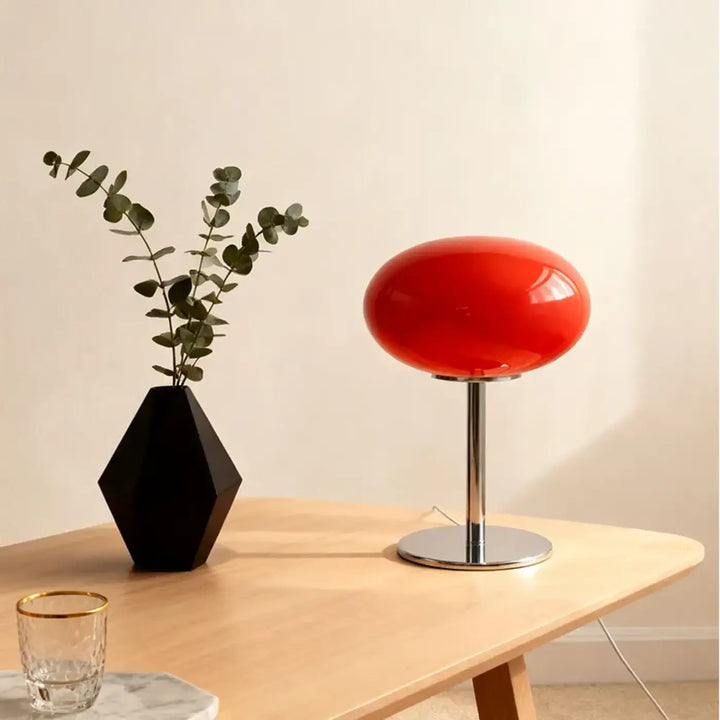 Lampe de chevet minimaliste en verre rouge ovale avec base et tige chrome, la lumière devient plus qu’un simple éclairage