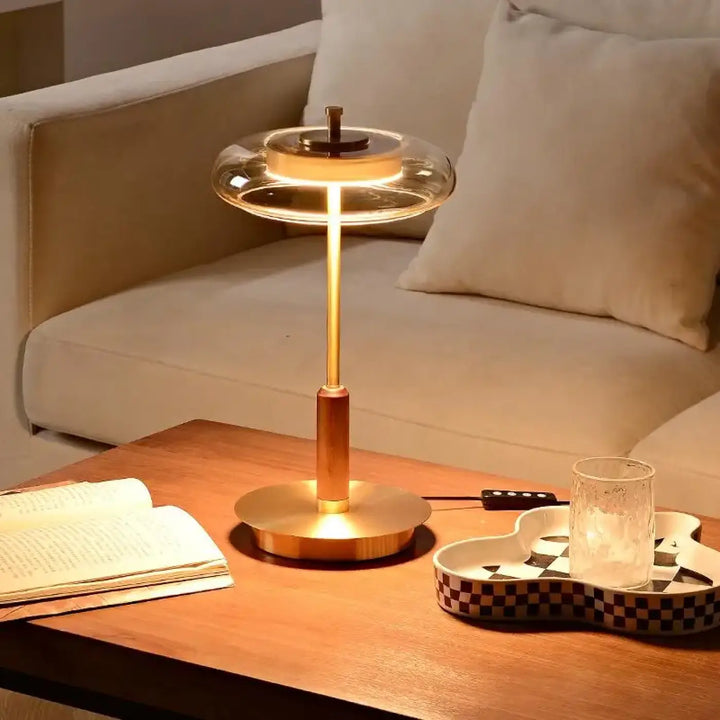 Lampe de chevet moderne cuivrée avec dôme en verre transparent et base circulaire émettant une lumière chaleureuse