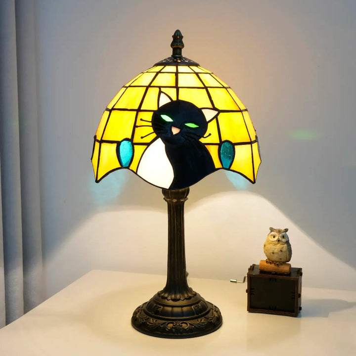 Lampe de chevet jaune en verre teinté avec chat noir et blanc aux yeux verts lumineux sur base bronze vintage pour ambiance chaleureuse et lumière douce
