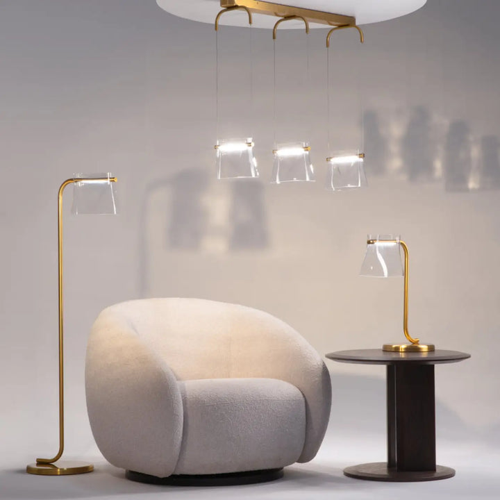 Fauteuil beige crème en tissu doux à design moderne arrondi présenté avec une lampe à poser en verre transparent aux lignes fluides