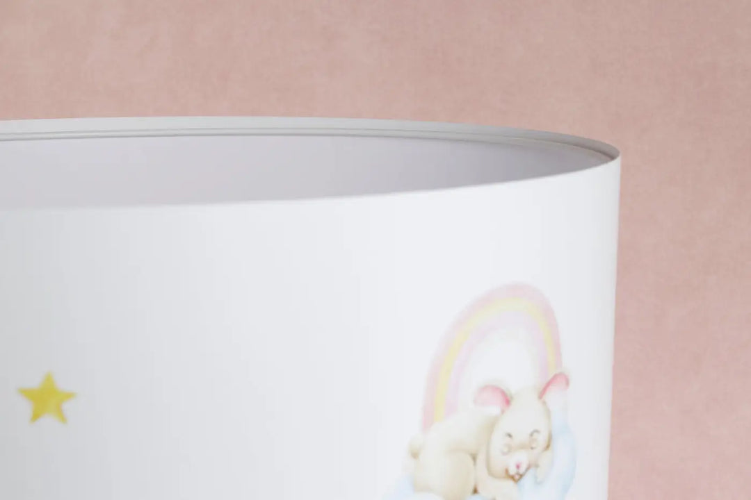 Lampe de table blanche avec abat-jour cylindrique illustré d’un ourson pleine crème sous un arc pastel
