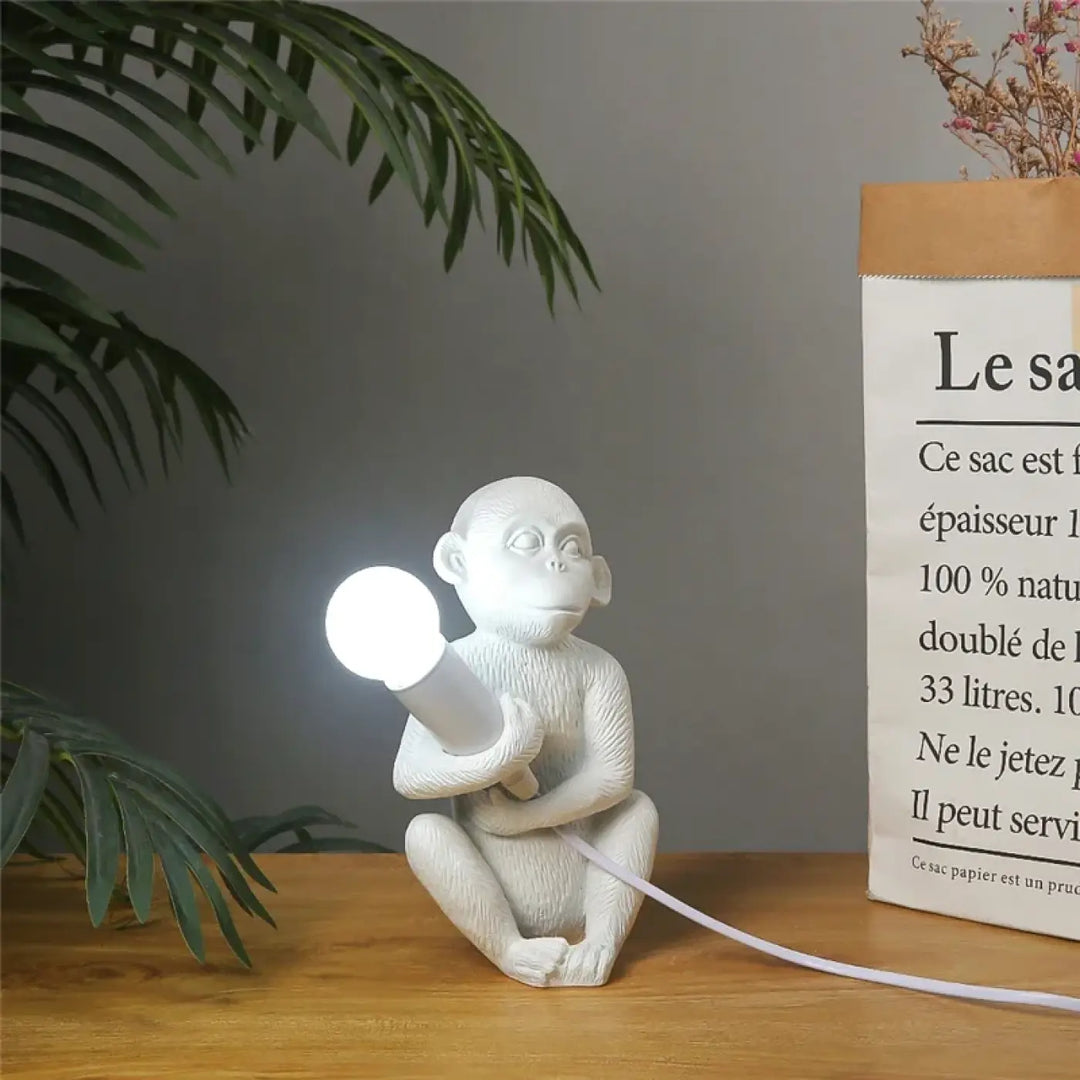 Lampe de table zaboo en céramique blanche avec singe assis sculptural tenant une ampoule lumineuse
