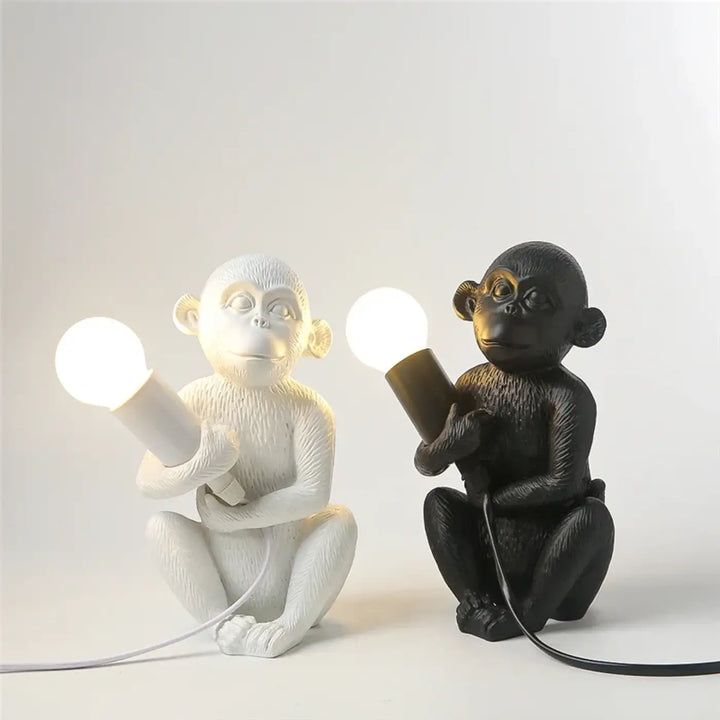 Lampe de table zaboo avec singe assis en résine blanche et noire tenant une ampoule lumineuse sculpturale singe assis