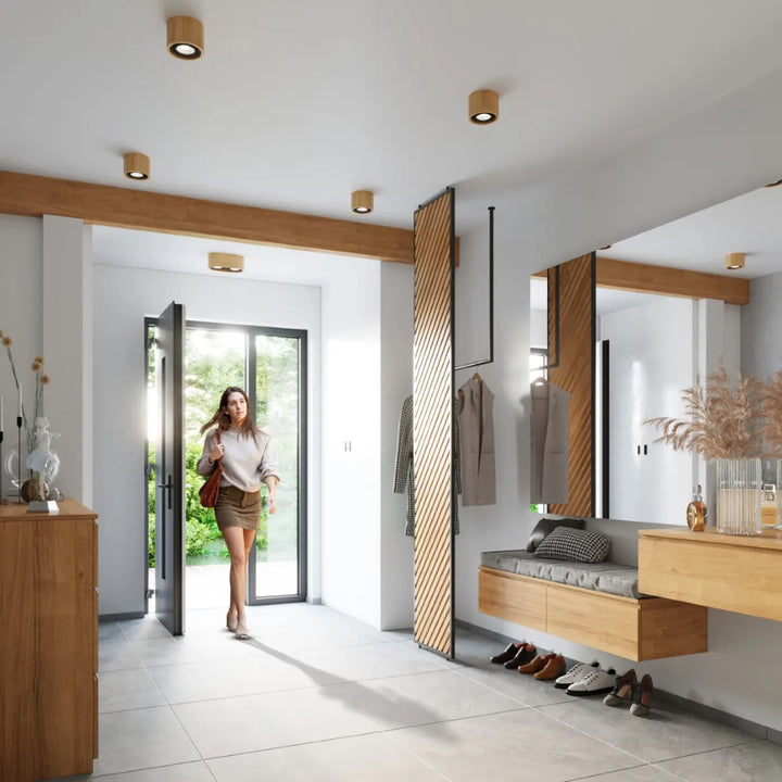 Une femme entre dans un hall moderne avec un sac en cuir brun sous un plafonnier basic en bois naturel sentez mieux