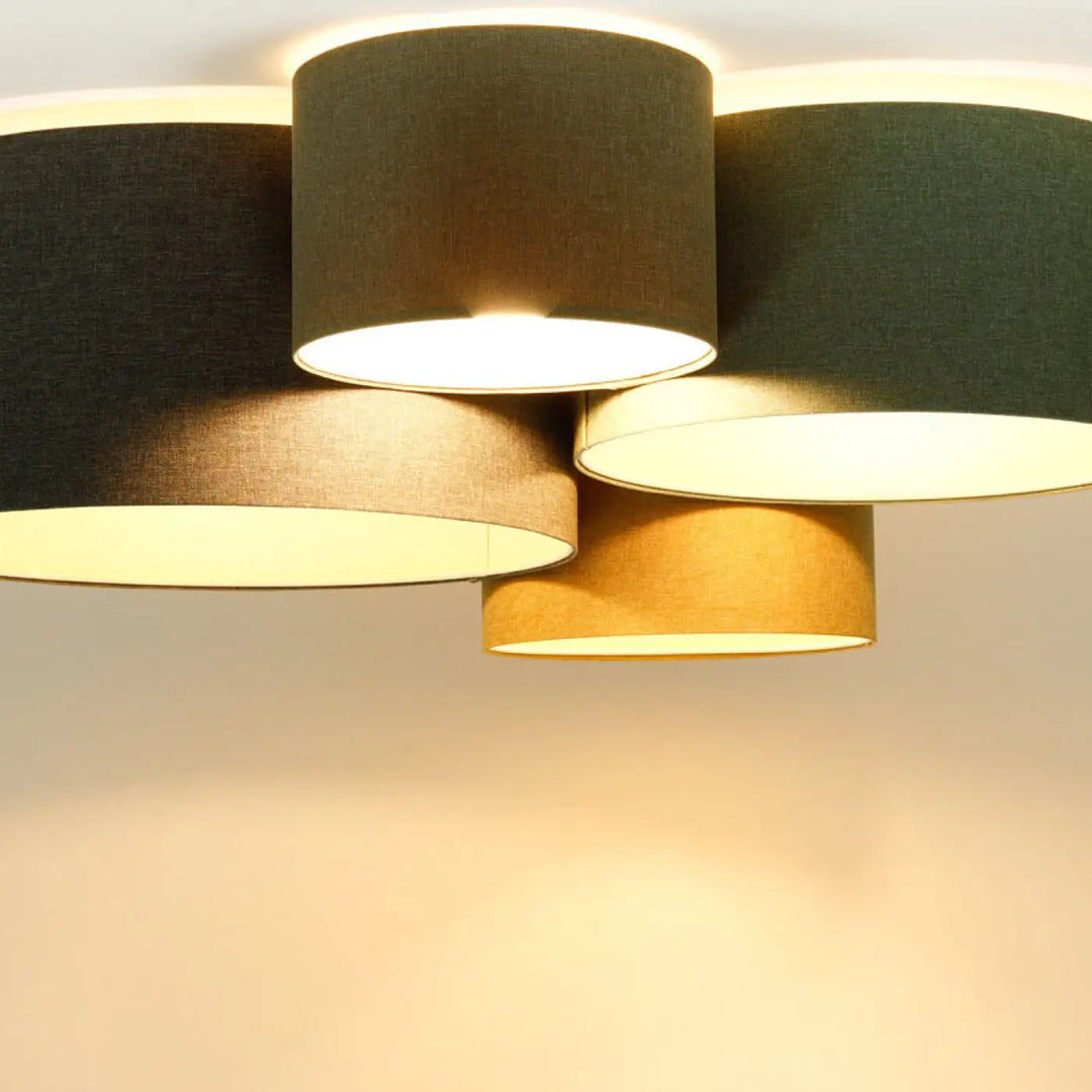 Luminaire plafonnier avec plusieurs abat-jours cylindriques en tissu gris marron et jaune moutarde émettant une lumière naturelle