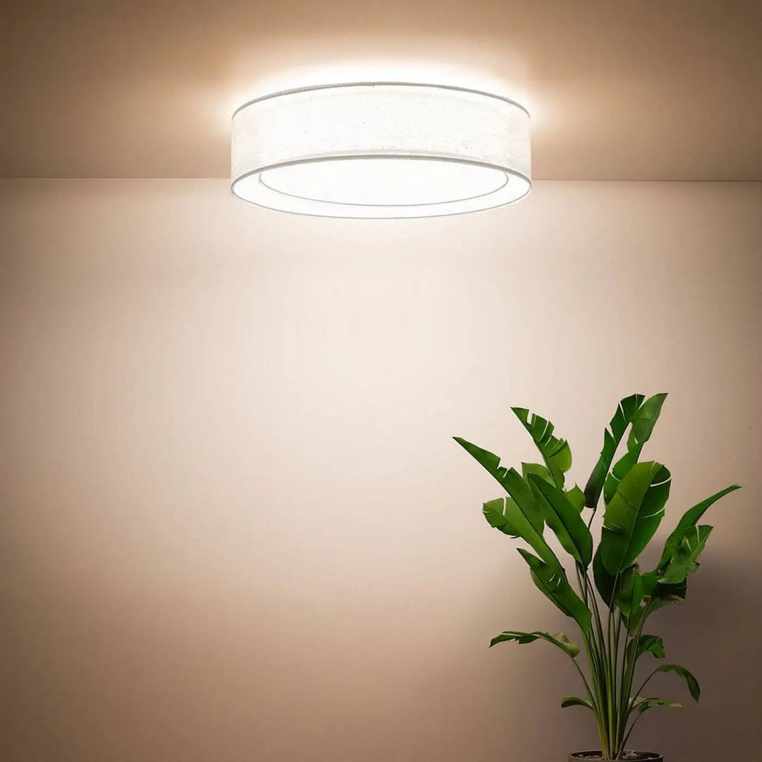 Luminaire plafonnier rond blanc avec abat-jour en tissu blanc et bord métallique émettant une lumière ambiante chaleureuse