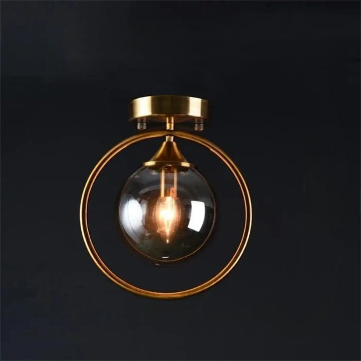 Luminaire plafonnier orbane avec anneau doré et boule lumineuse en verre clair et ampoule à filament exposé
