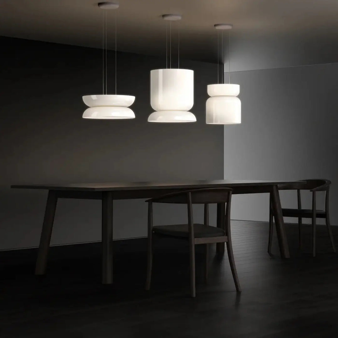 Luminaire plafonnier totem pablo designs avec trois suspensions blanches en verre opale soufflé au-dessus d’une table en bois
