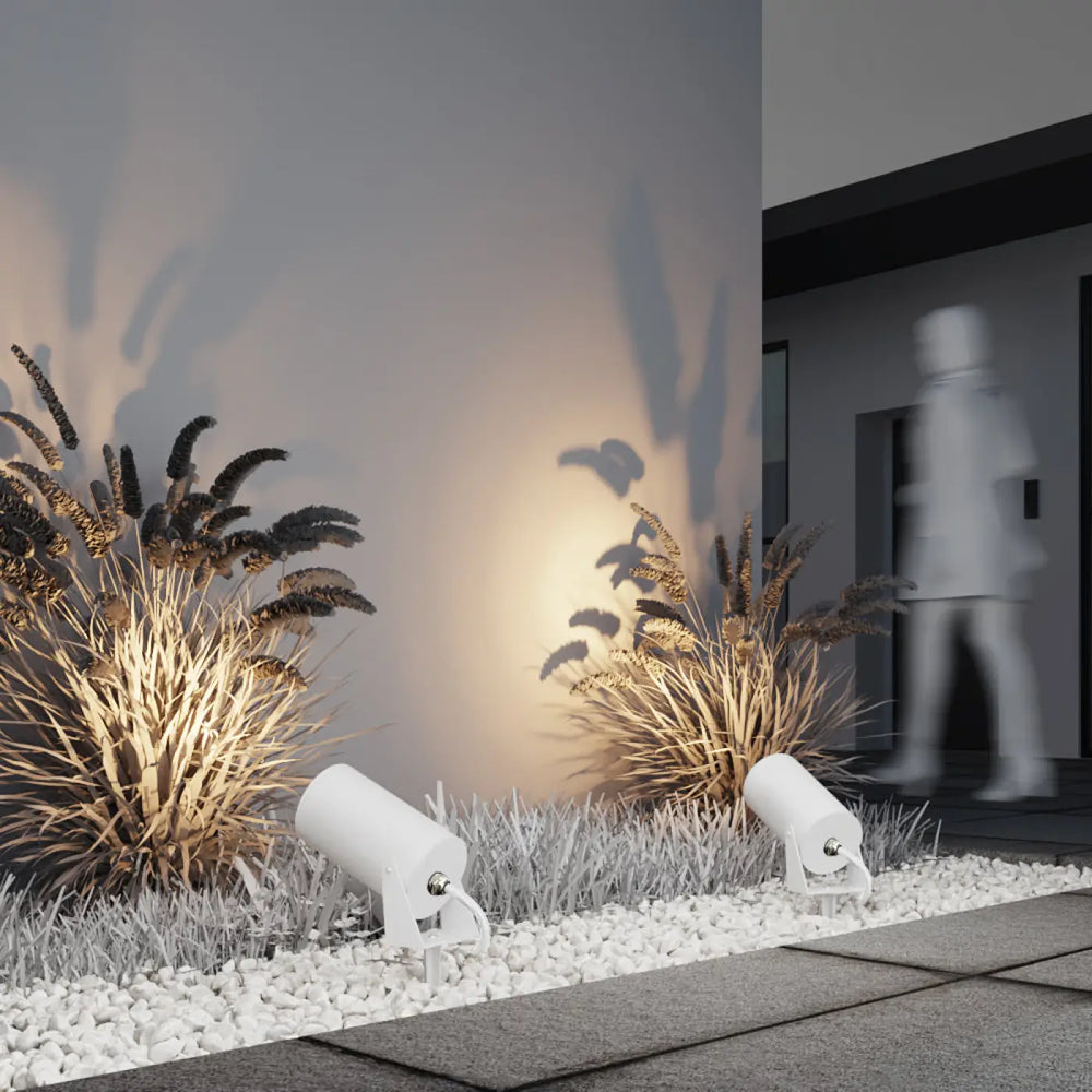 Deux spots piquet extérieur blancs cylindriques avec tête orientable intégrés dans des galets blancs bern