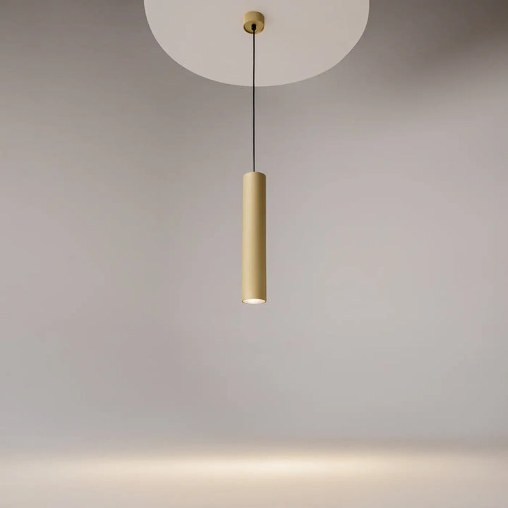 Suspension artisan cylindrique au-dessus d’une table avec finition mate dorée et design minimaliste