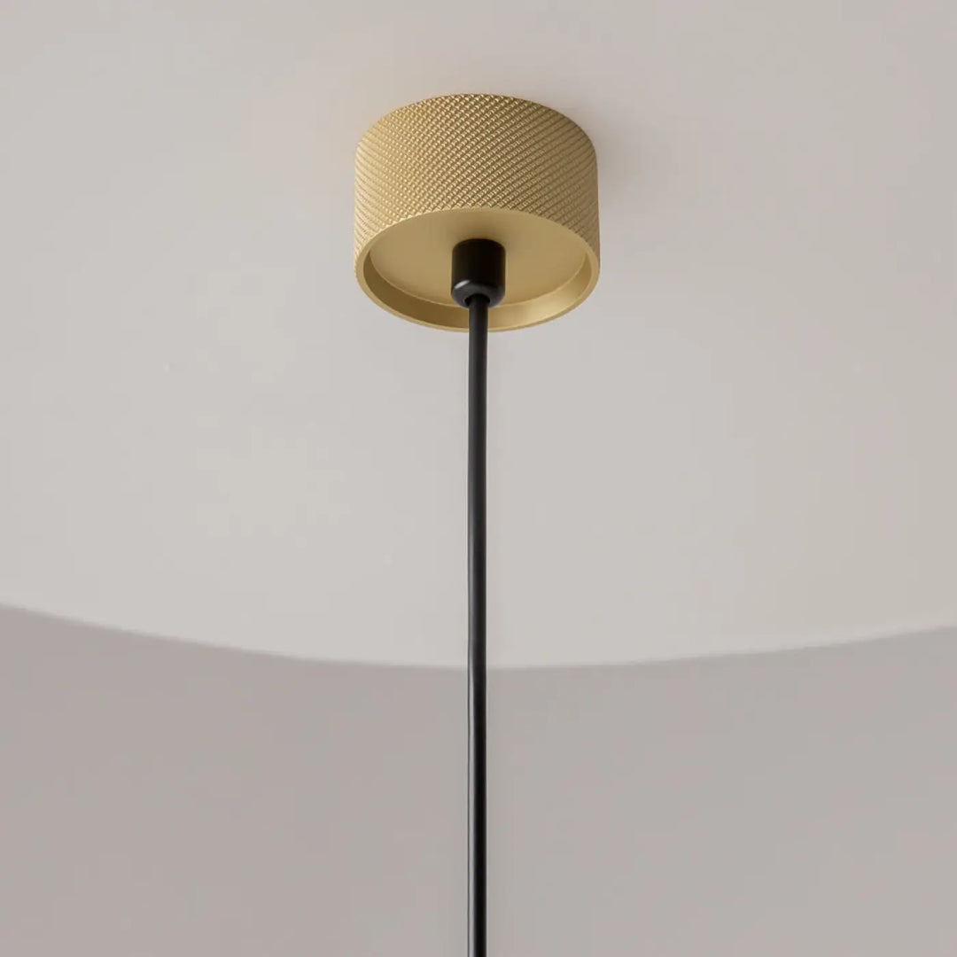 Suspension artisan dorée au-dessus d’une table avec surface texturée en diamant et câble noir en tissu