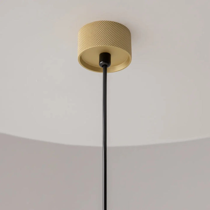 Suspension artisan dorée au-dessus d’une table avec surface texturée en diamant et câble noir en tissu
