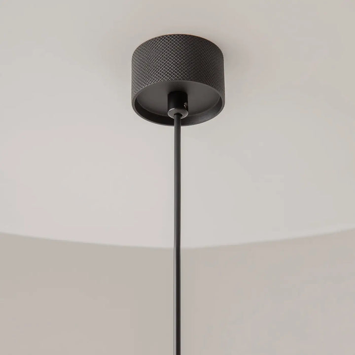 Suspension artisan noire avec finition mate et design cylindrique au-dessus d’une table pour un éclairage élégant