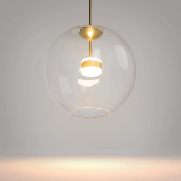 Suspension cometa avec verre soufflé sphérique et fixation en laiton avec led intégrée au-dessus d’une table