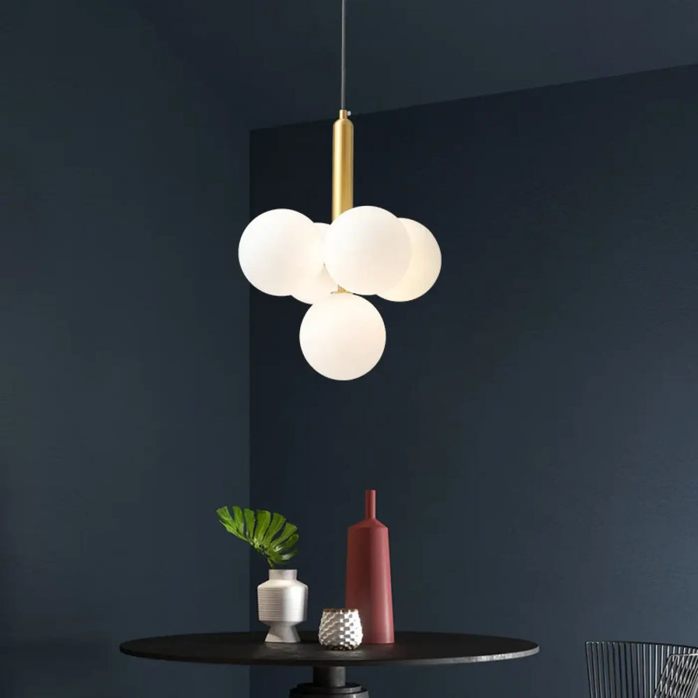 Suspension luminaire dinah avec tige métal doré et quatre sphères en verre blanc rond givré design moderne
