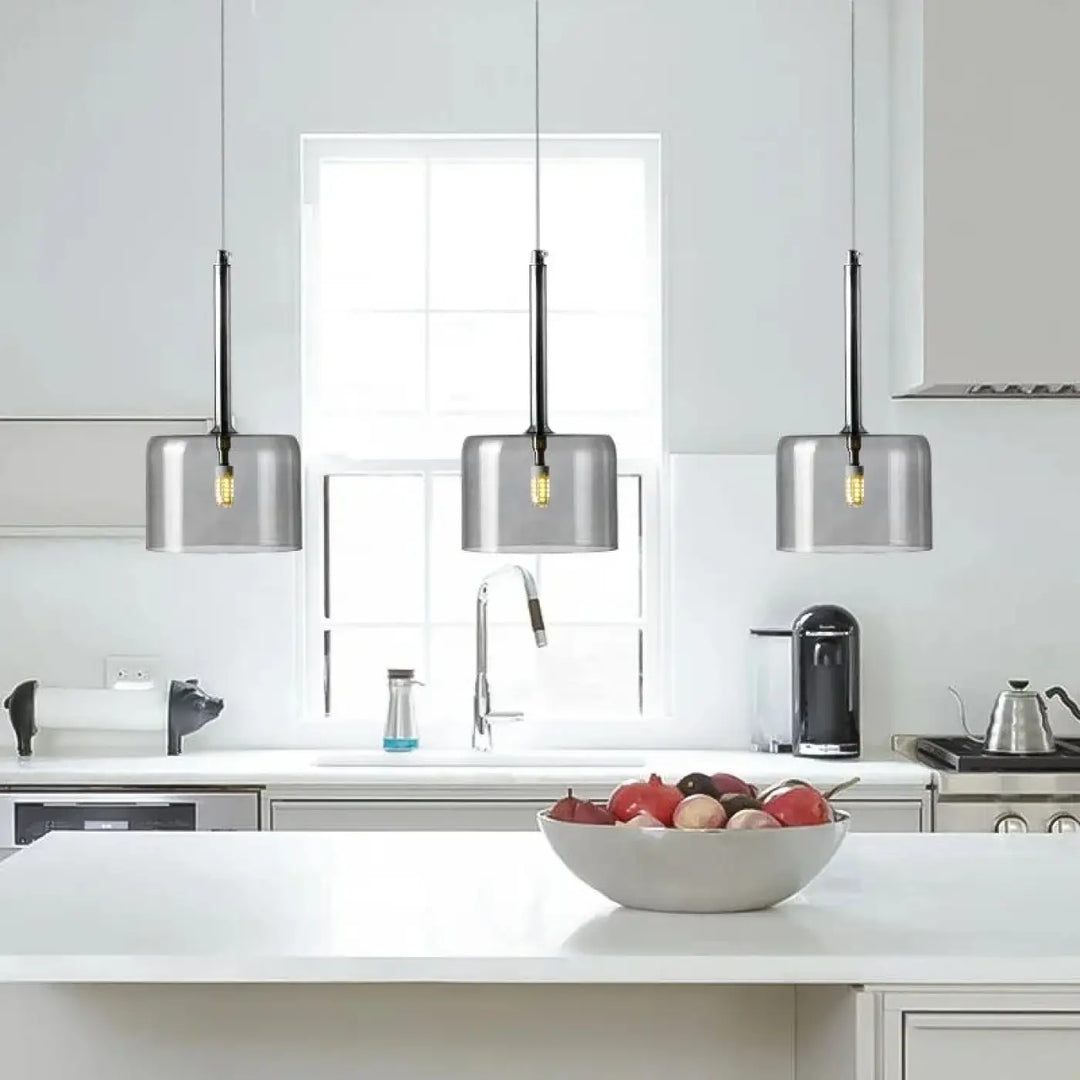 Suspension luminaire cylis avec abat jours cylindriques en verre gris translucide et cordons noirs au-dessus dîlot cuisine blanc