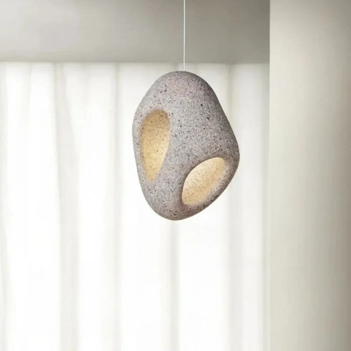 Suspension luminaire cavia en pierre grise tachetée avec deux découpes ovales laissant filtrer une lumière chaude