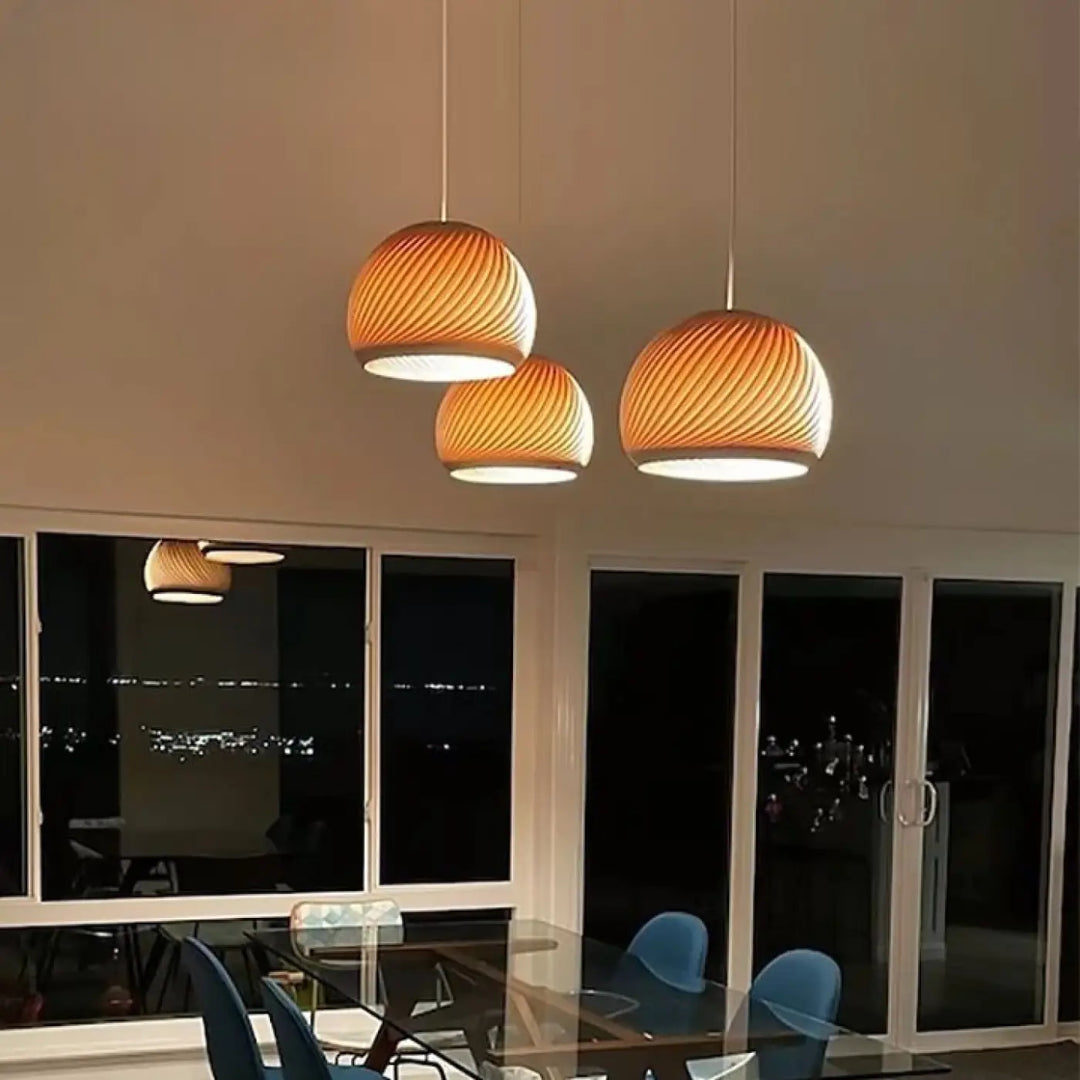 Trois suspensions luminaires en bois aux formes ribées de ton chaud suspendues au plafond dans le design luvia