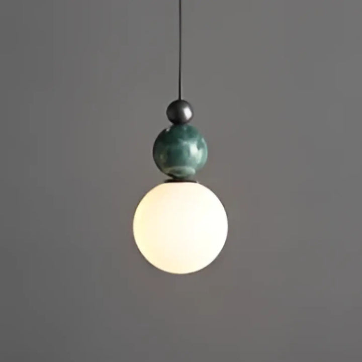Suspension luminaire eluna avec design moderne featuring orbe céramique vert mat au-dessus d’un globe en verre blanc