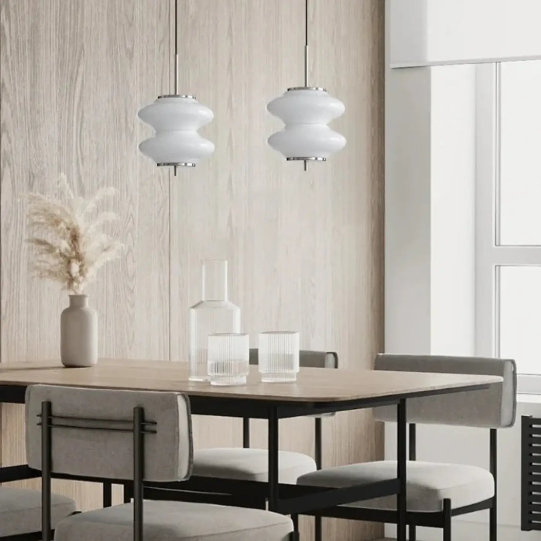 Deux suspensions luminaires en verre blanc en formes arrondies avec fixations métalliques au-dessus d’une table à manger