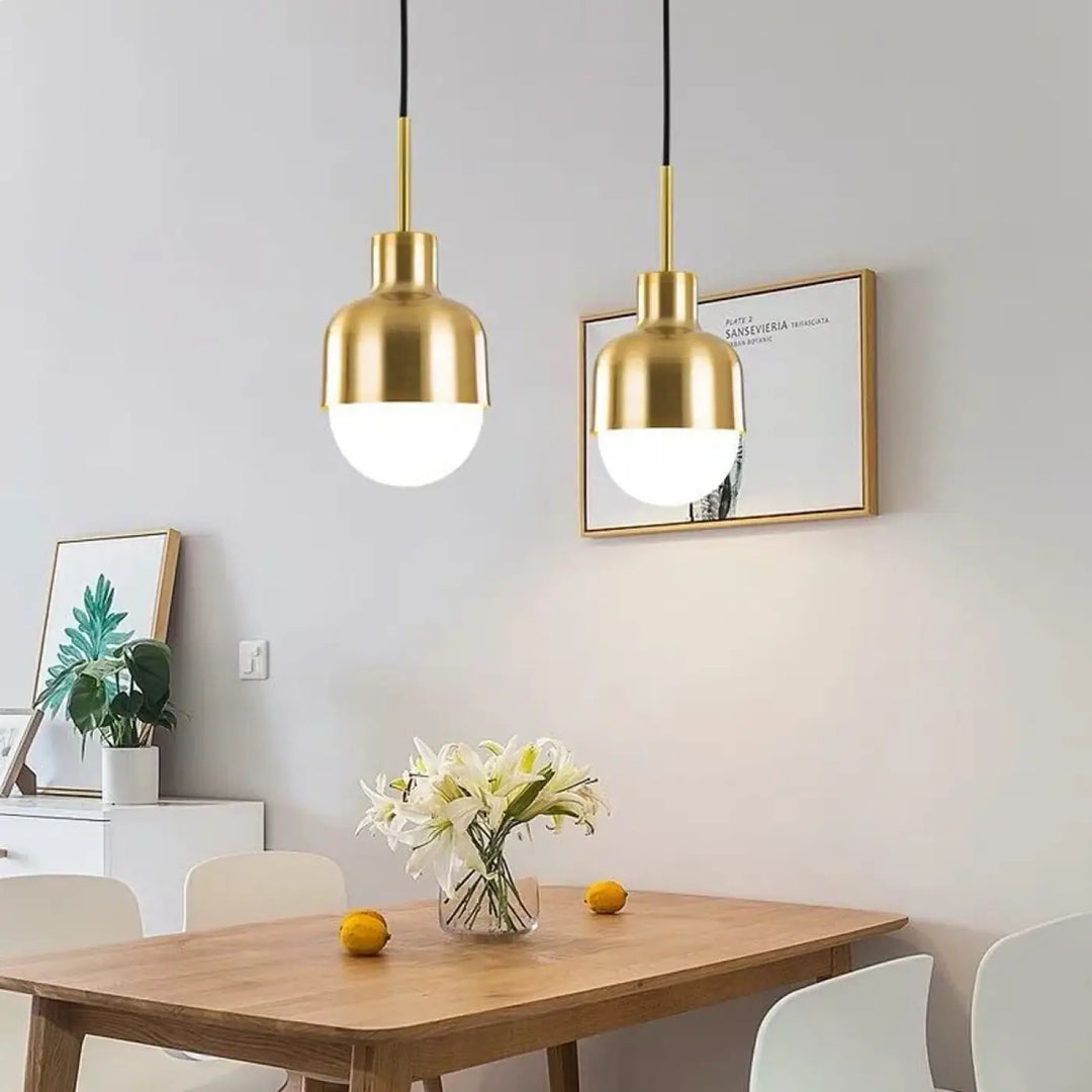Deux suspensions luminaires avec finition dorée et abat-jours en verre dépoli au-dessus d’une table en bois