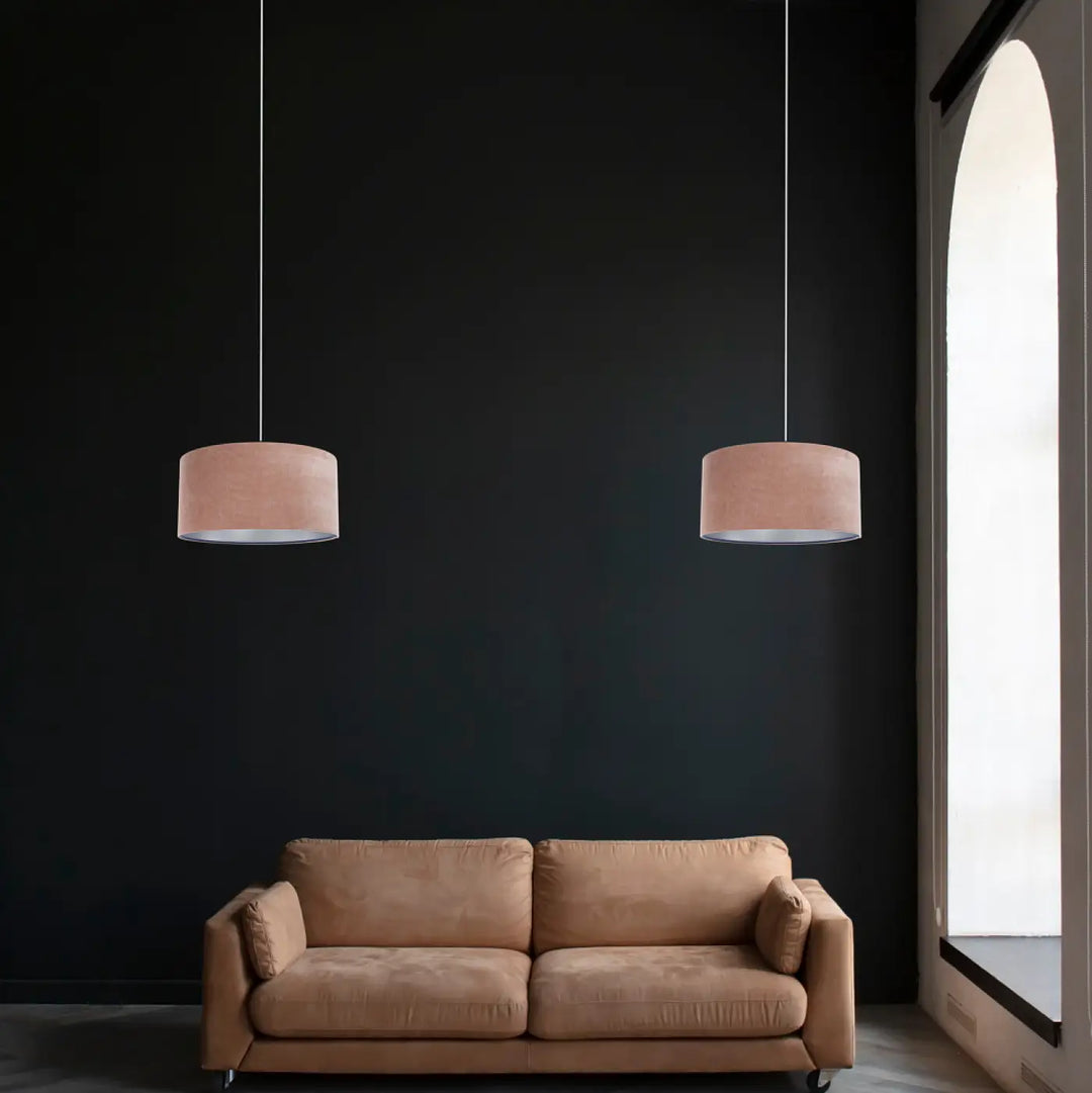 Deux suspensions luminaires cylindriques en tissu rose blush style moderne chic suspendues devant un mur sombre