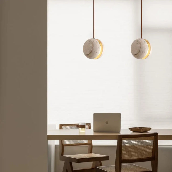 Suspension luminaire kreto avec abat-jours en béton texturé et accents halo doré au-dessus d’une table en bois travertin aux lignes