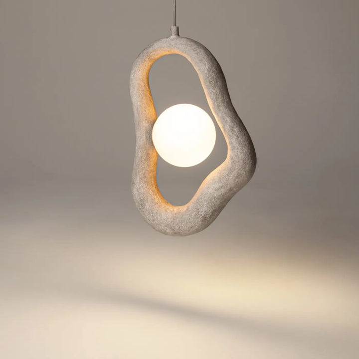 Suspension opus en béton gris avec cadre ovale à volume irrégulier et lumière douce émanant d’une ampoule sphérique blanche