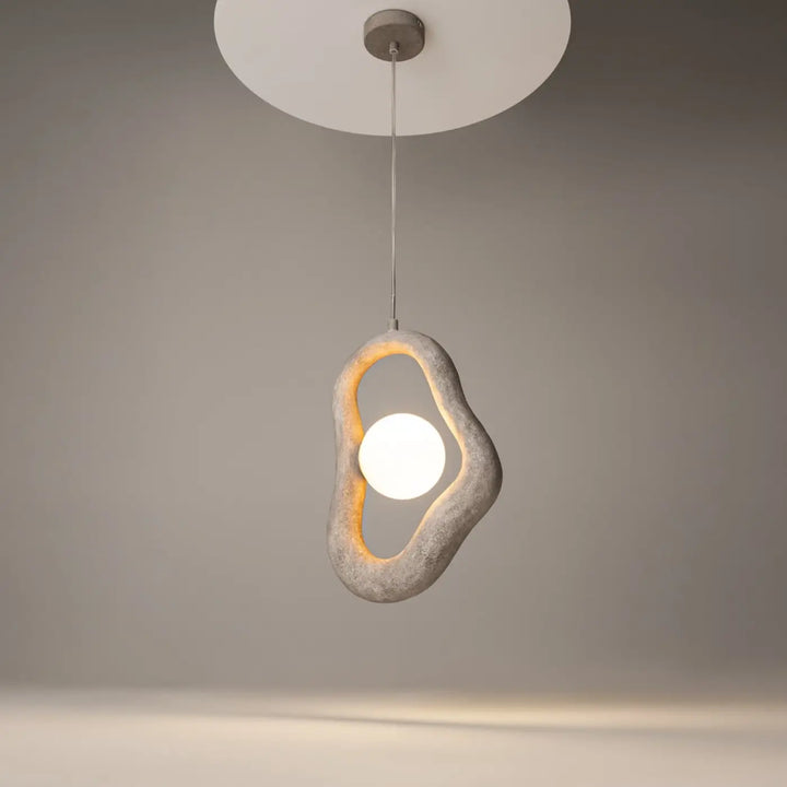 Suspension opus en béton gris texturé avec volume irrégulier entourant une lumière douce blanche