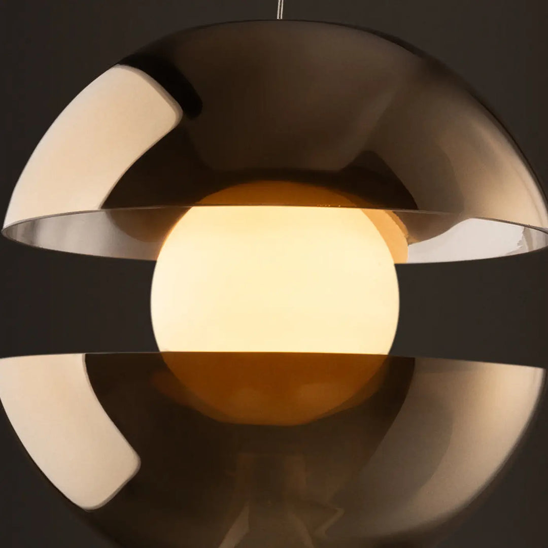 Suspension rebel sphérique moderne en chrome poli avec verre ambré au-dessus d’une table éclairant d’une lueur chaude