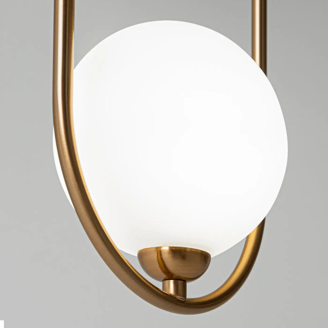 Suspension ring art déco avec globe sphérique en verre blanc mat et bras métalliques ton laiton au-dessus d’un îlot